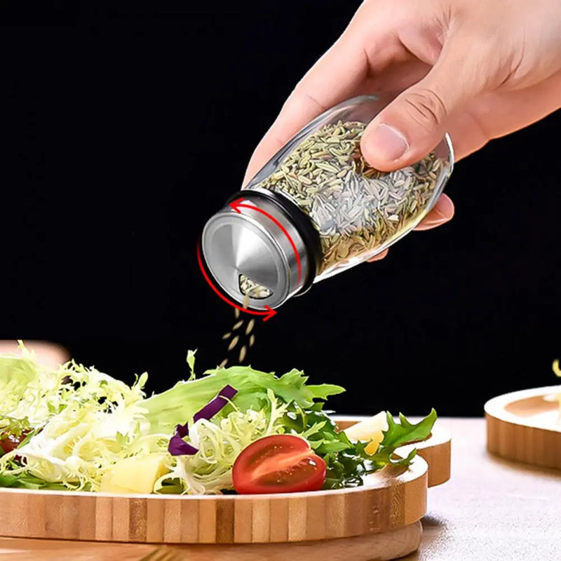 Hand sprinkling dried herbs from clear glass spice jar onto a salad on a wooden salad plate