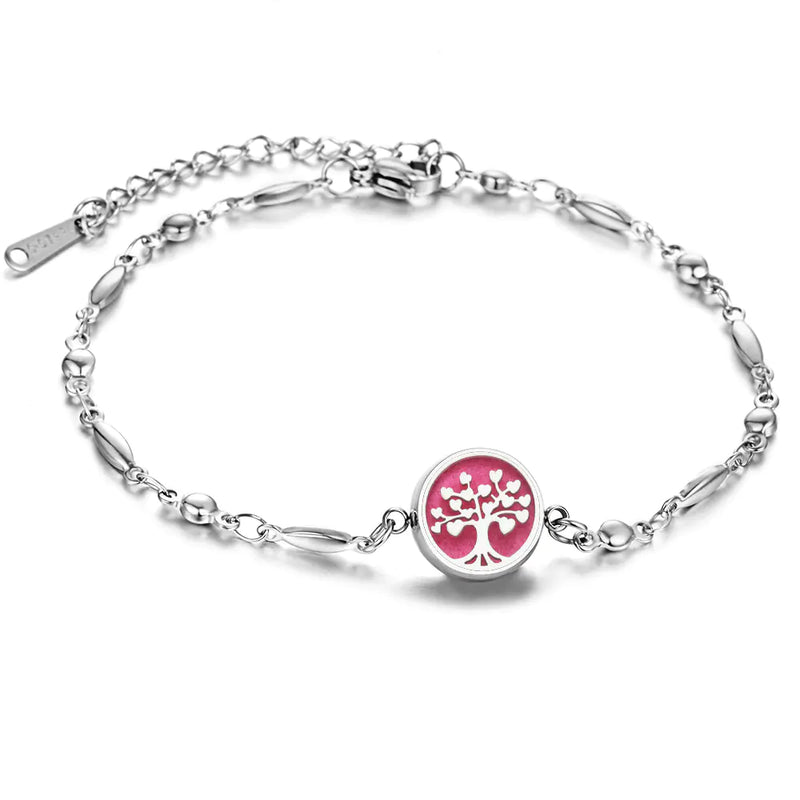 Silver colored bracelent with small round design that shows a tree with leaves and roots in front of pink background, Has place to add drops of essential oil for fragrance
