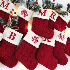 Red Christmas stockings style crew socks with snowflake and Letter design, surrounded by festive decorations.