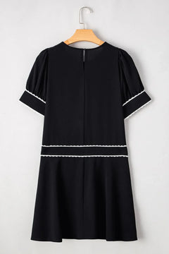 Black dress with white trim on a hanger against a white background