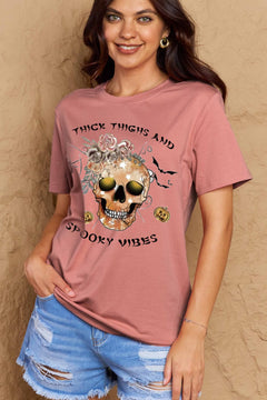 Pink t-shirt with a skull surrounded by small Jackolanterns, batts, flowers and a spider. The text Reads Thick Thighs and Spooky Vibes
