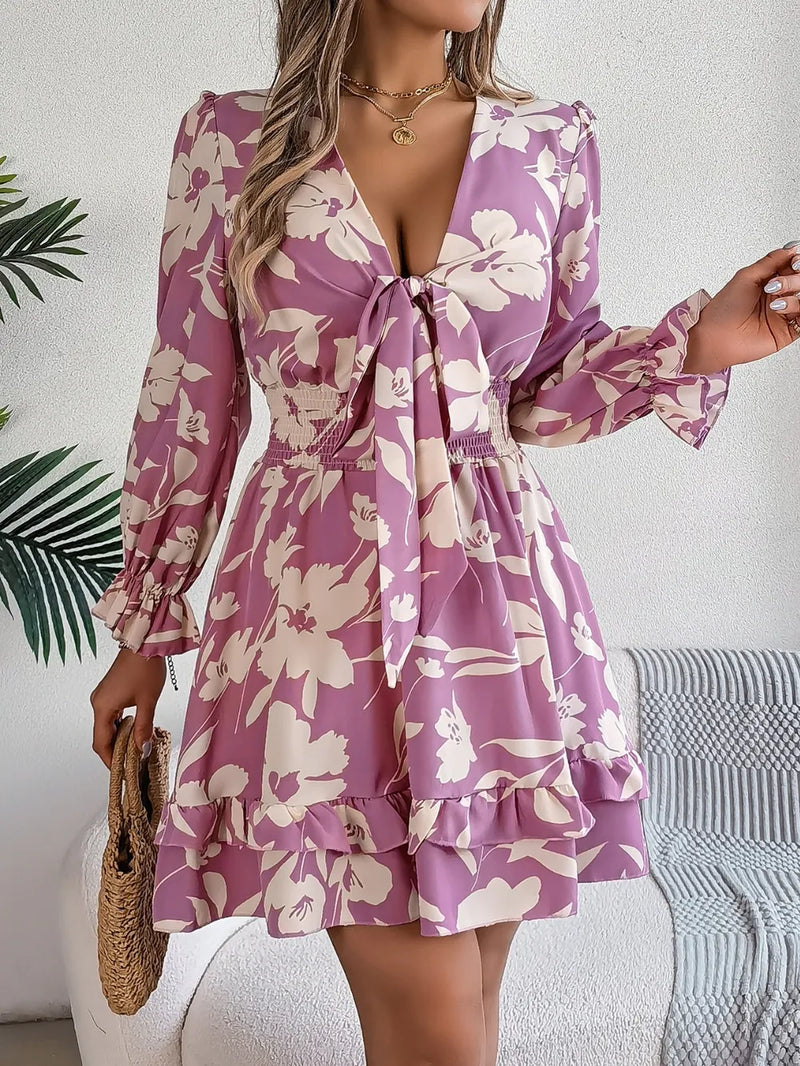 Woman wearing a purple floral dress with long sleeves in a minimal indoor setting.