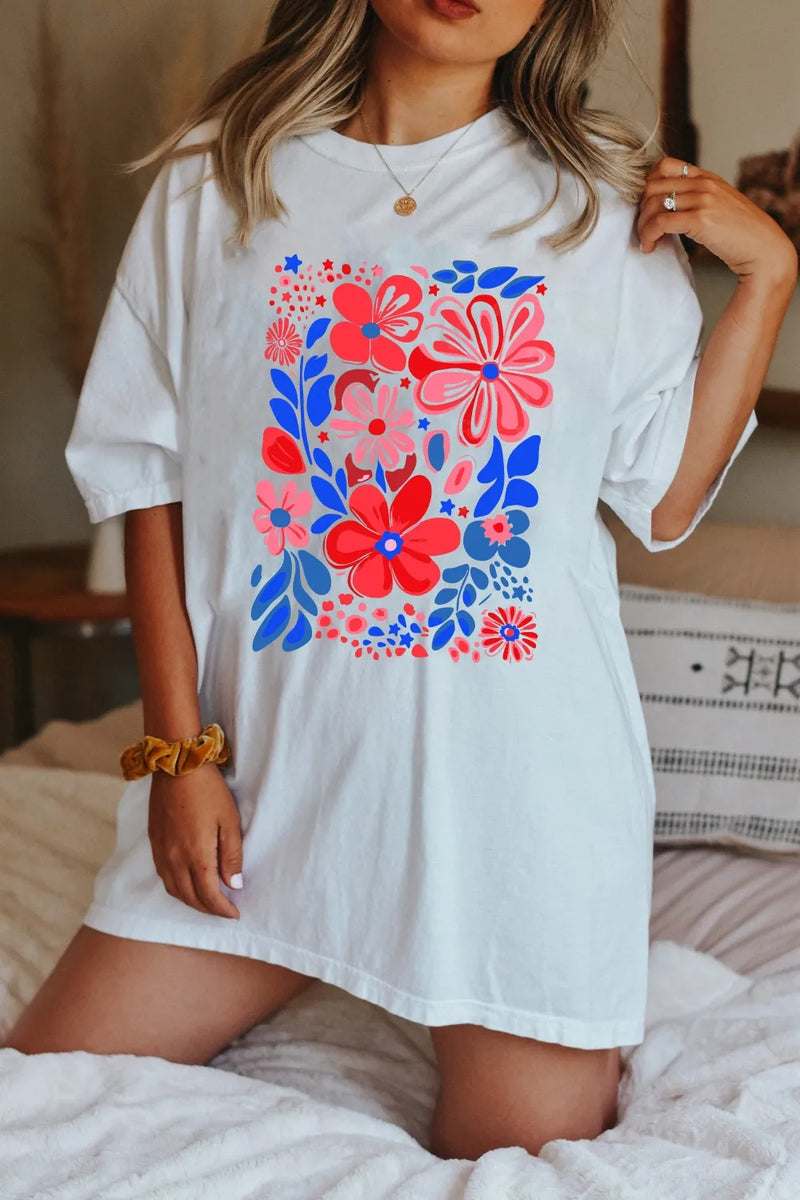 Person wearing a white oversized t-shirt with colorful floral design sitting on a bed.