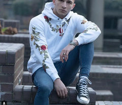 Person wearing a white hoodie with floral embroidery sitting on steps.