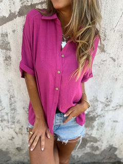 Person wearing a bright pink shirt and denim shorts against a textured wall.