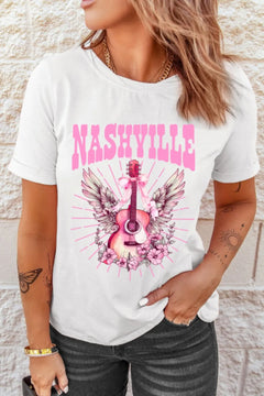 Creamy white Tshirt with short sleeves and round neck, the design is a Guitar standing on end, with the arm pointing up. There is a pink bow tied towards the top with long ribbon ends flowing down, pink and white wings extend out behind the guitar and the bottom is nestled in pink flowers that look similar to a carolina rose.Extending out all around the design are straight pink lines which imply rays of light. The caption above the design is in Pink Capital letters and says NASHVILLE