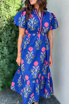 Floral Puff Short Sleeve Notched High Waist Dress with Royal blue background and large bold pink blooming flowers on green stems with smaller flowers and buds on each side of the bigger ones, in purple and orangy-red. full skirt with an extra panel to give an almost tiered look.  Pink and blue trim around the neck and down the front to the waist.