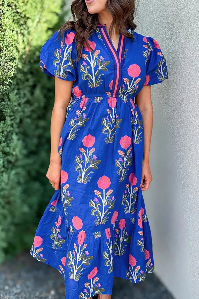 Floral Puff Short Sleeve Notched High Waist Dress with Royal blue background and large bold pink blooming flowers on green stems with smaller flowers and buds on each side of the bigger ones, in purple and orangy-red. full skirt with an extra panel to give an almost tiered look.  Pink and blue trim around the neck and down the front to the waist.