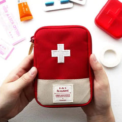 Red first aid pouch with a white cross held by hands on a white background