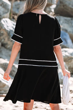 Woman wearing a black dress with white trim standing on rocky terrain.