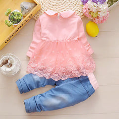 Pink lace top and blue jeans set on a light wooden floor with decorative items.