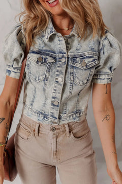 Short waisted, short sleeved, denim jacket with button up front and buttoned pockets on the chest. Faded blue color.