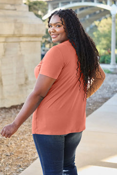 Woman wearing a rust-colored shirt and blue jeans standing outdoors.