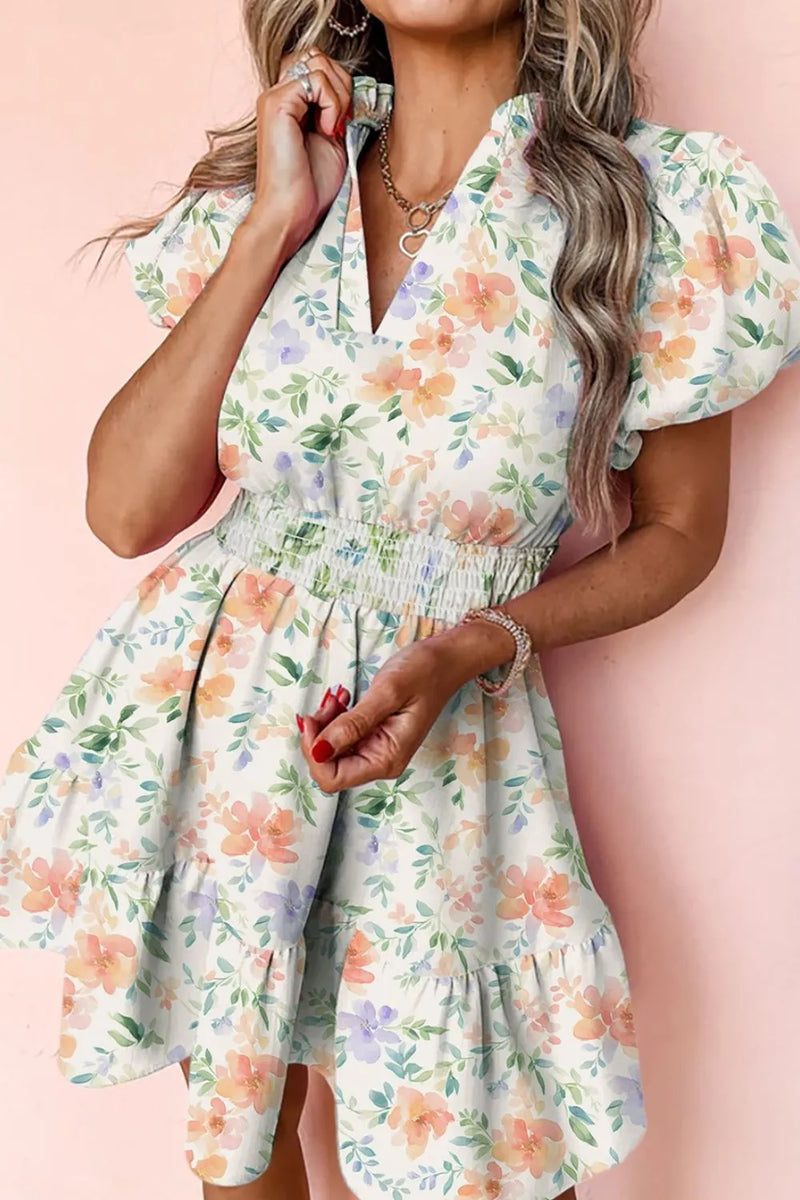 Frill Notched Puff Sleeve Dress with elastic gathered waist and ruffled skirt. The dress is wite with impressionistic style flowers in peach, and blue, with green leaves and stems