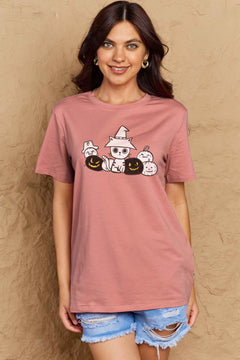Woman wearing a pink t-shirt with Halloween-themed design against a beige wall.