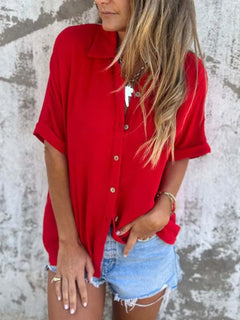 Person wearing a red shirt and denim shorts against a textured wall.