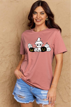 Woman wearing a pink t-shirt with Halloween-themed design against a beige wall.