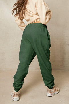 Person wearing green sweatpants and a beige top against a beige background