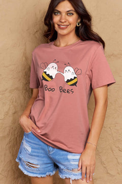 Woman wearing a pink t-shirt with 'Boo Bees' graphic design against a beige wall.