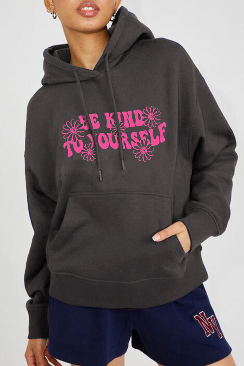 A black hoodie with pink block letters stating BE KIND TO YOURSELF with pink flowers around the words.Handwarmer pocket on front, pullover