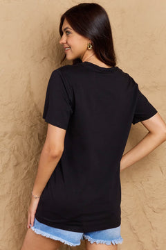 Woman wearing a black t-shirt and denim shorts against a beige wall
