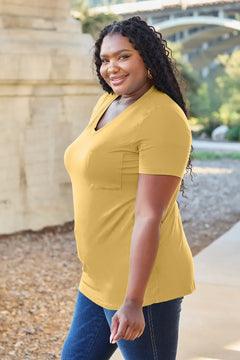 Woman wearing a yellow top and blue jeans standing outdoors with a bridge in the background