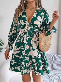 Woman wearing a green floral dress holding a straw bag indoors.
