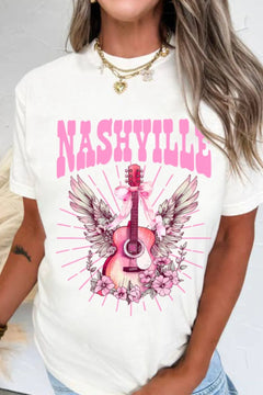 Creamy white Tshirt with short sleeves and round neck, the design is a Guitar standing on end, with the arm pointing up. There is a pink bow tied towards the top with long ribbon ends flowing down, pink and white wings extend out behind the guitar and the bottom is nestled in pink flowers that look similar to a carolina rose.Extending out all around the design are straight pink lines which imply rays of light. The caption above the design is in Pink Capital letters and says NASHVILLE