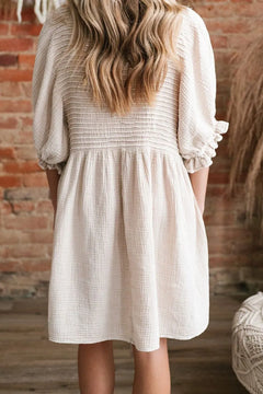 Person wearing a white dress with long sleeves in front of a brick wall.