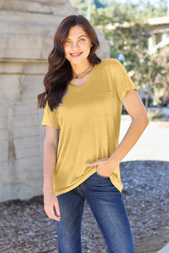 Woman wearing a mustard yellow t-shirt and blue jeans standing outdoors.