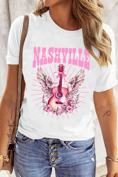 Creamy white Tshirt with short sleeves and round neck, the design is a Guitar standing on end, with the arm pointing up. There is a pink bow tied towards the top with long ribbon ends flowing down, pink and white wings extend out behind the guitar and the bottom is nestled in pink flowers that look similar to a carolina rose.Extending out all around the design are straight pink lines which imply rays of light. The caption above the design is in Pink Capital letters and says NASHVILLE