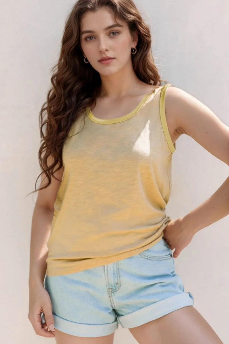 Woman wearing a yellow tank top and light blue shorts against a plain background