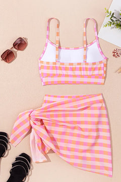 Pink and orange checkered bikini top and skirt set on a beige background with sunglasses and black shoes.
