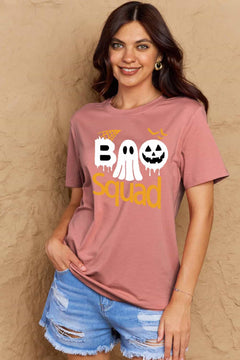 Pink round neck tshirt with short sleeves. Hallowee Theme with the word Boo but the first o is a sheet ghost and the second o is a white jack o'lantern and below that is the word Squad in orange. Above the B is an orange spider web and above the pumpkin are three orange flying bat silhouttes
