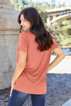 Woman wearing a pink t-shirt and blue jeans standing outdoors.