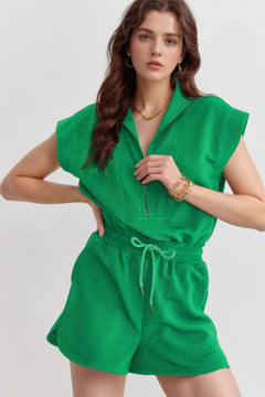 A green shorts romper with very short sleeves and collar with zipper down the front. Drawstring at the waist and side pockets.