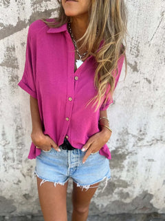 Person wearing a bright pink shirt and denim shorts against a textured wall.