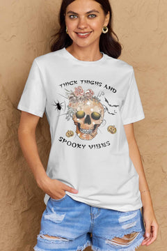 White t-shirt with a skull surrounded by small Jackolanterns, batts, flowers and a spider. The text Reads Thick Thighs and Spooky Vibes