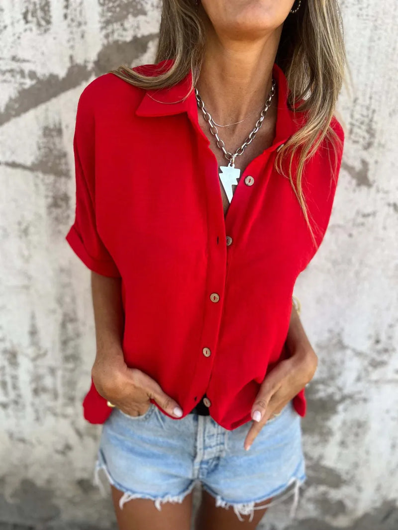 Person wearing a red shirt and denim shorts against a textured wall.