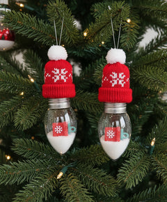 Two light bulb-shaped ornaments with decorative items inside hanging from a Christmas tree