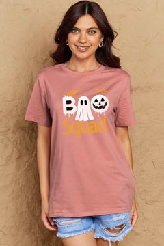 Pink round neck tshirt with short sleeves. Hallowee Theme with the word Boo but the first o is a sheet ghost and the second o is a white jack o'lantern and below that is the word Squad in orange. Above the B is an orange spider web and above the pumpkin are three orange flying bat silhouttes