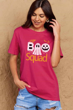 Pink round neck tshirt with short sleeves. Hallowee Theme with the word Boo but the first o is a sheet ghost and the second o is a white jack o'lantern and below that is the word Squad in orange. Above the B is an orange spider web and above the pumpkin are three orange flying bat silhouttes
