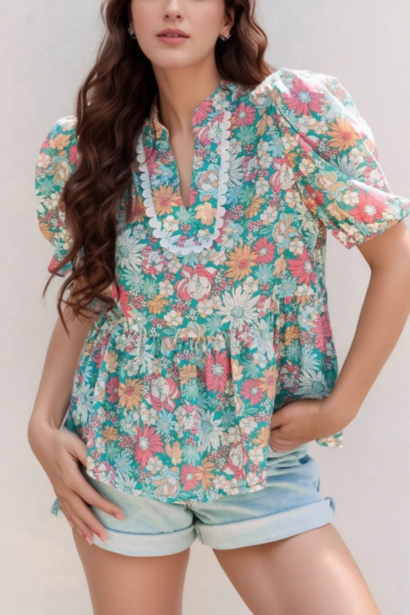 Multicolour Notched Neck Puff Short Sleeve Floral Blouse with almost a turquoise background and mostly covered with all types of pink, white, orange, blue and other shades of flowers. white scalloped border around the notched portion of the neck front.