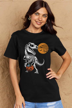 black short sleeved t-shirt with a dinosaur skeleton design on front. Dinosaur is holding a trick or treat jack o'lantern basket with candy in it and looking back at an orange moon with the silhouttes of bats and tree branches in front of it