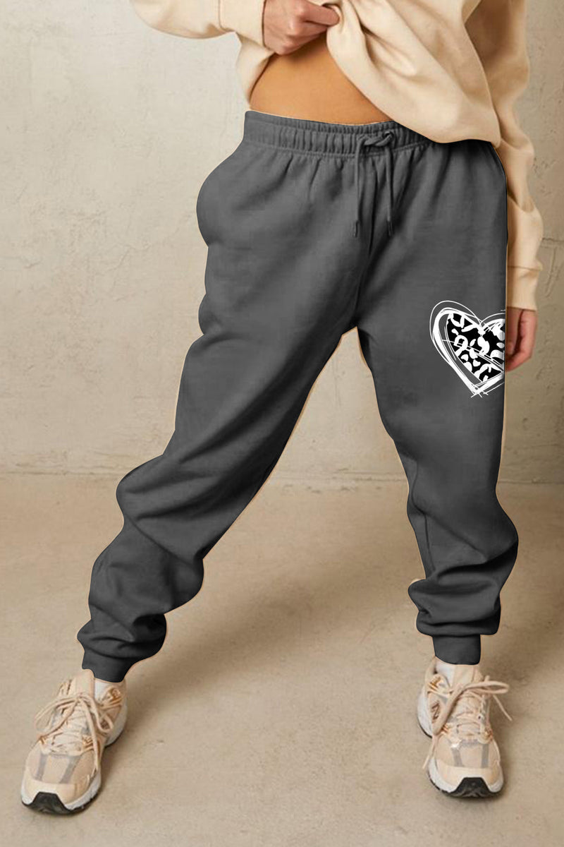 Person wearing gray sweatpants with a heart-shaped design on a beige background