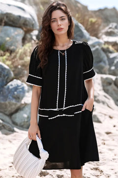 Woman in a black dress with white trim standing on a rocky beach.