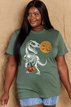 Green short sleeved t-shirt with a dinosaur skeleton design on front. Dinosaur is holding a trick or treat jack o'lantern basket with candy in it and looking back at an orange moon with the silhouttes of bats and tree branches in front of it