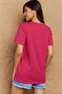 Woman wearing a pink t-shirt and denim shorts against a beige wall