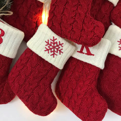 Red Christmas stockings style crew socks with snowflake and letter design, surrounded by festive decorations.