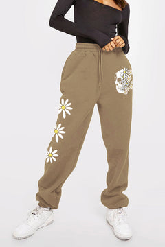 Khaki sweatpants with white skull partially obscured by daisys on left leg near the hip, and three large white daisys going down the other leg at thigh, knee and shin.